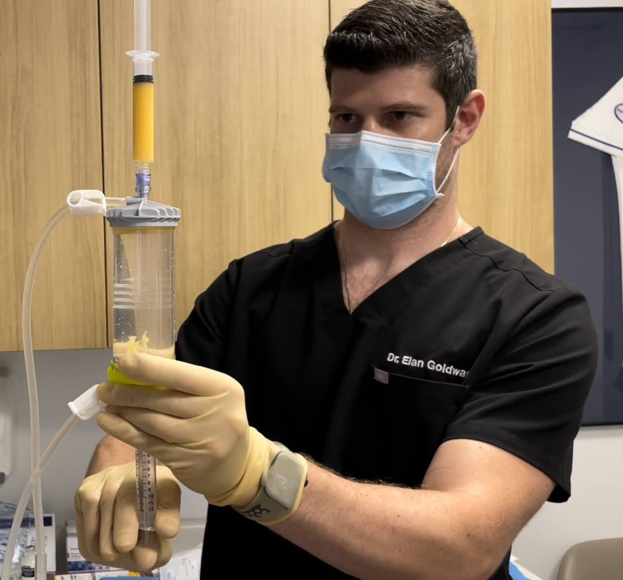 Dr. Goldwaser in black scrubs holding a Lipogems canister with prepared adipose tissue