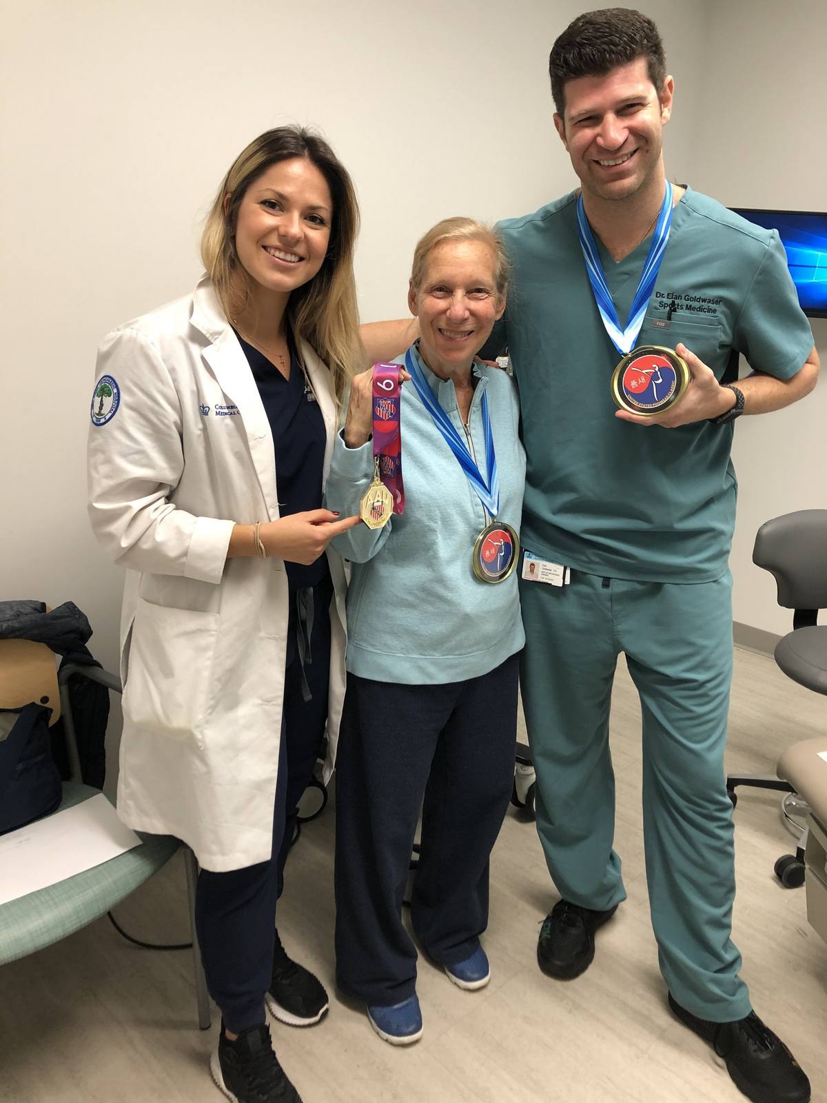A patient holding karate tournament medals with Dr. Goldwaser and a member of the care team