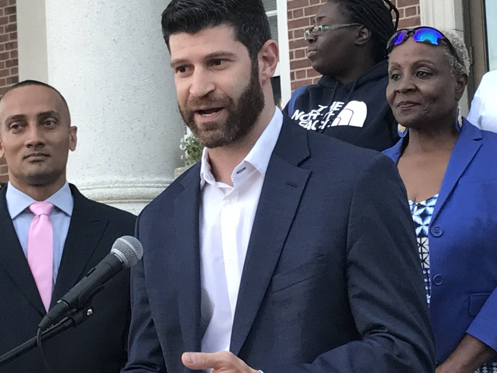Dr. Goldwaser speaking into a microphone on the steps of New Rochelle’s municipal building